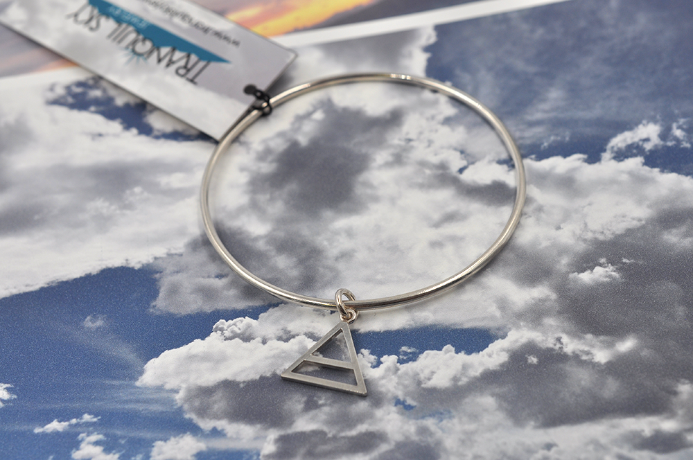 Pictured here is a round sterling silver bangle bracelet with a small air charm hanging from the continuous circle. Air symbol in a triangle with a line through the center. 