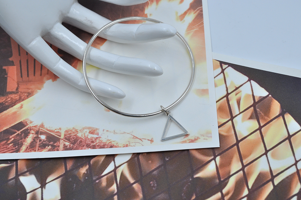 Round sterling silver continuous bangle braclet is showing laying on a mannequin hand's fingertips showcasing a dainty triangle indicative of the fire symbol.   