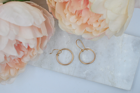 Gold round drop hoop earrings that measure approximately one inch in width pictured from above..